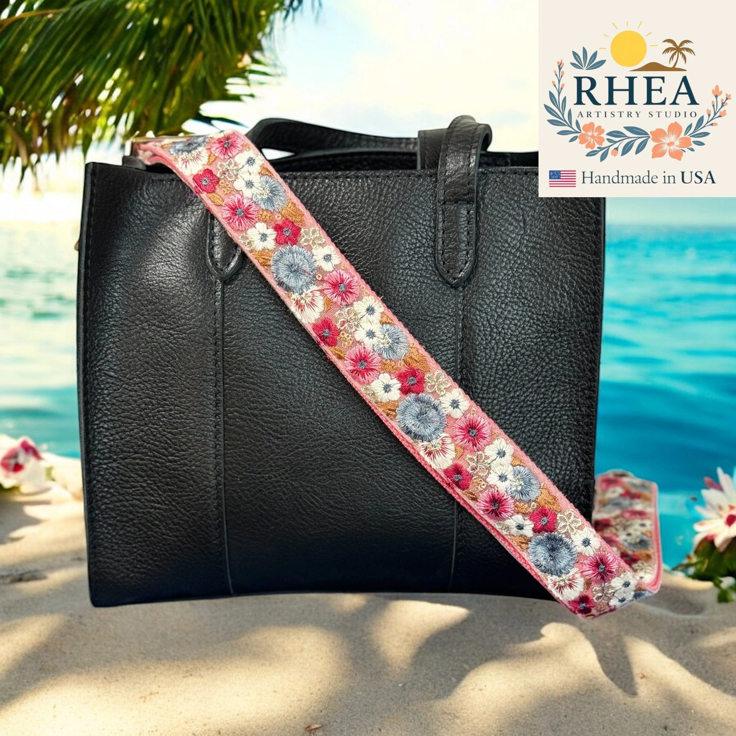 Black handbag with a floral purse strap against a bright blue background, featuring the Rhea Artistry Studio logo.
