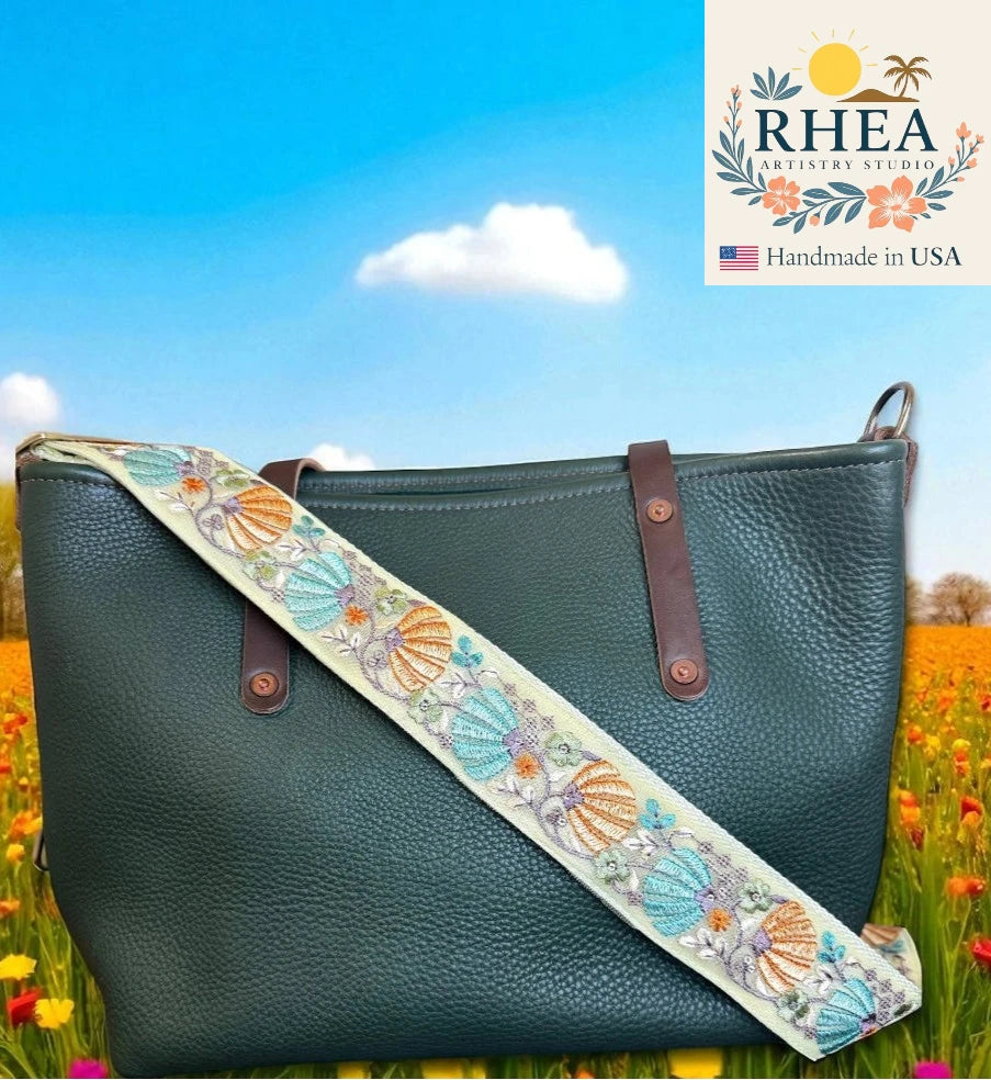 Green handbag with an embroidered strap against a scenic background, featuring the RHEA Artistry Studio logo.