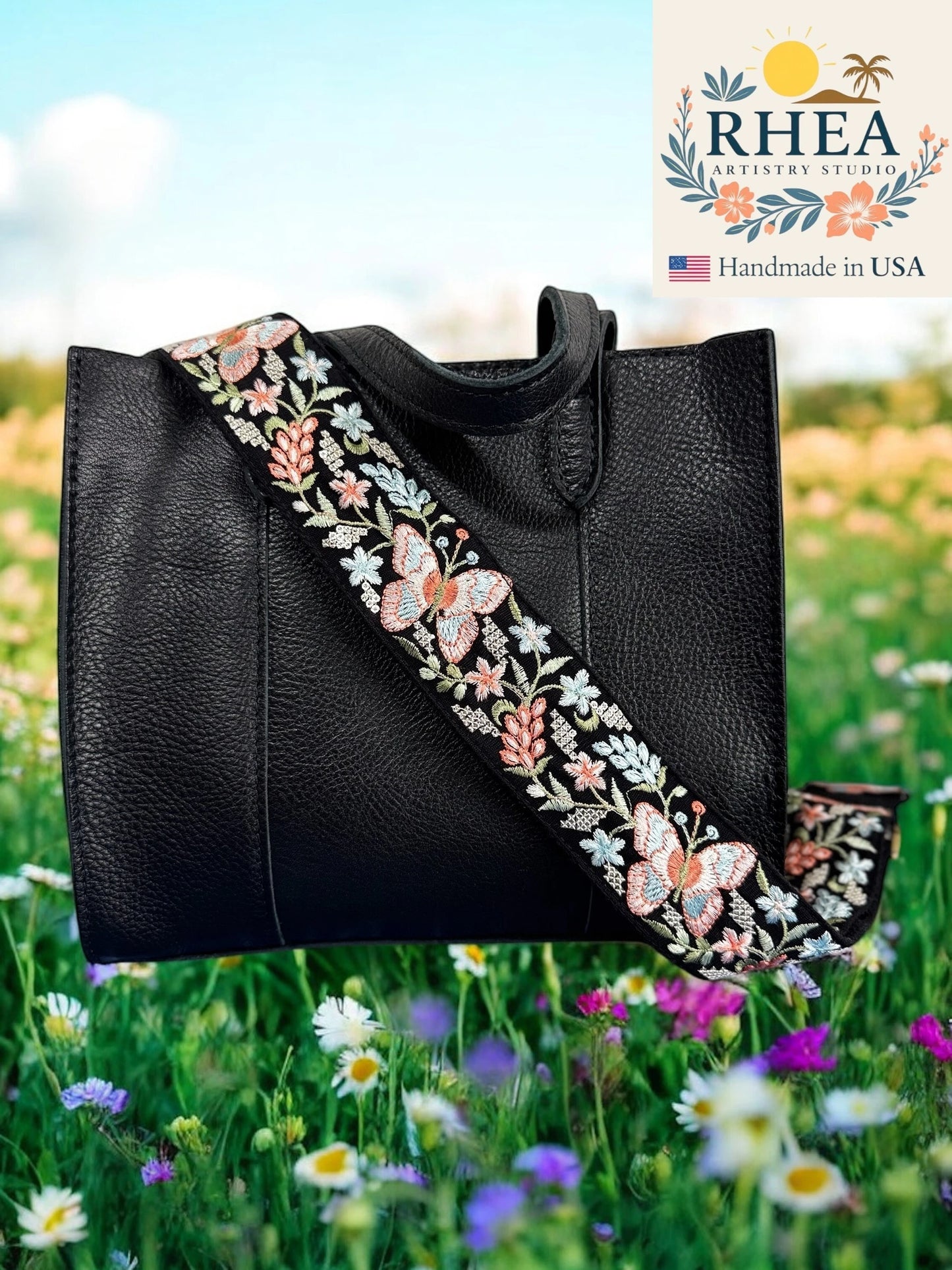 Black leather tote bag with floral embroidery purse strap in a field of flowers, featuring the RHEA brand.