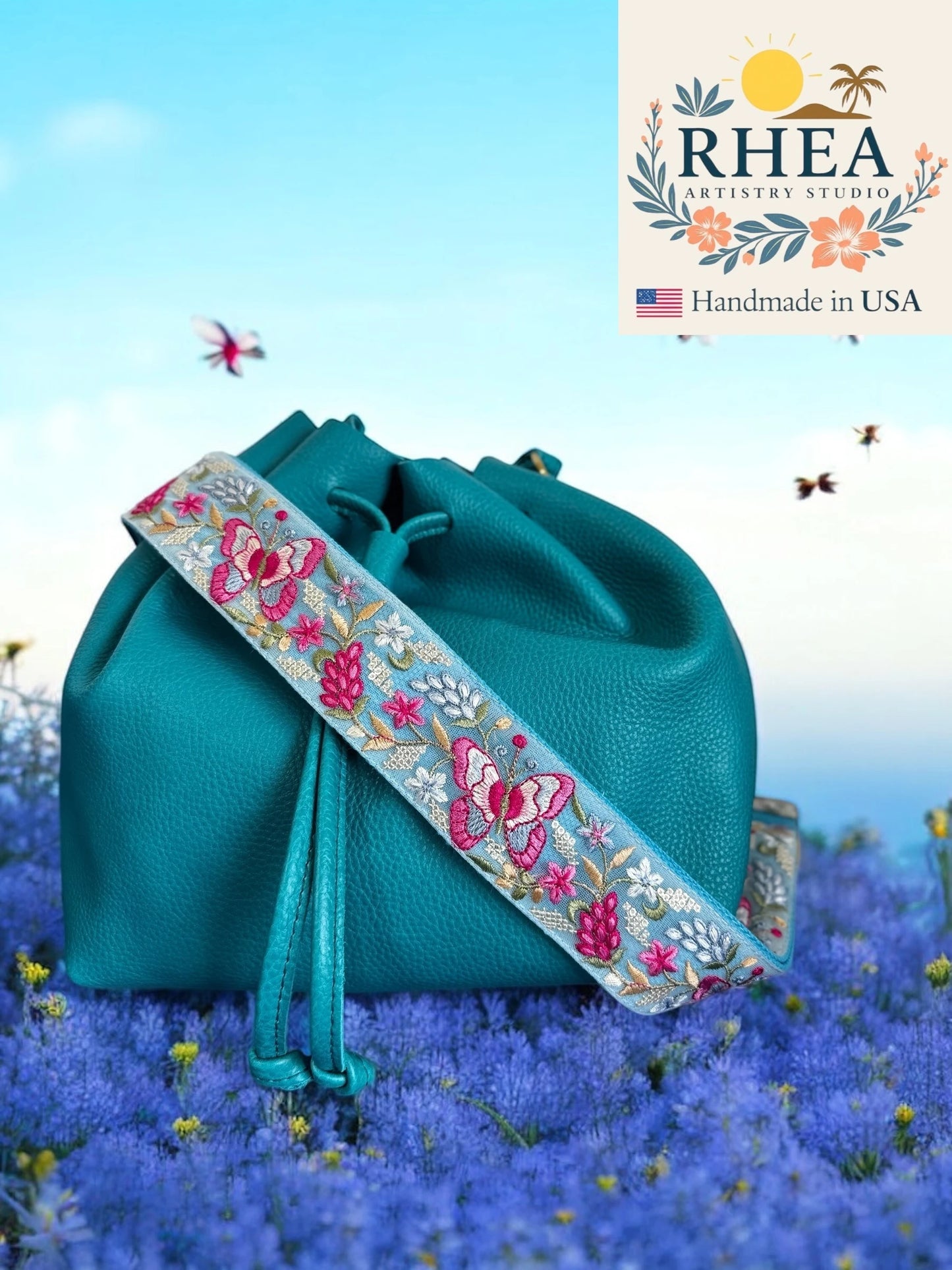 Teal handbag with embroidered purse strap on a blue floral background, featuring Rhea Artistry Studio logo.