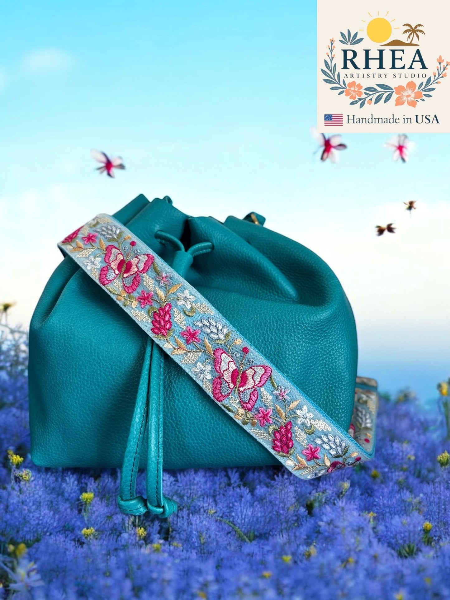 Teal handbag with floral purse strap on a blue background, featuring the RHEA brand.