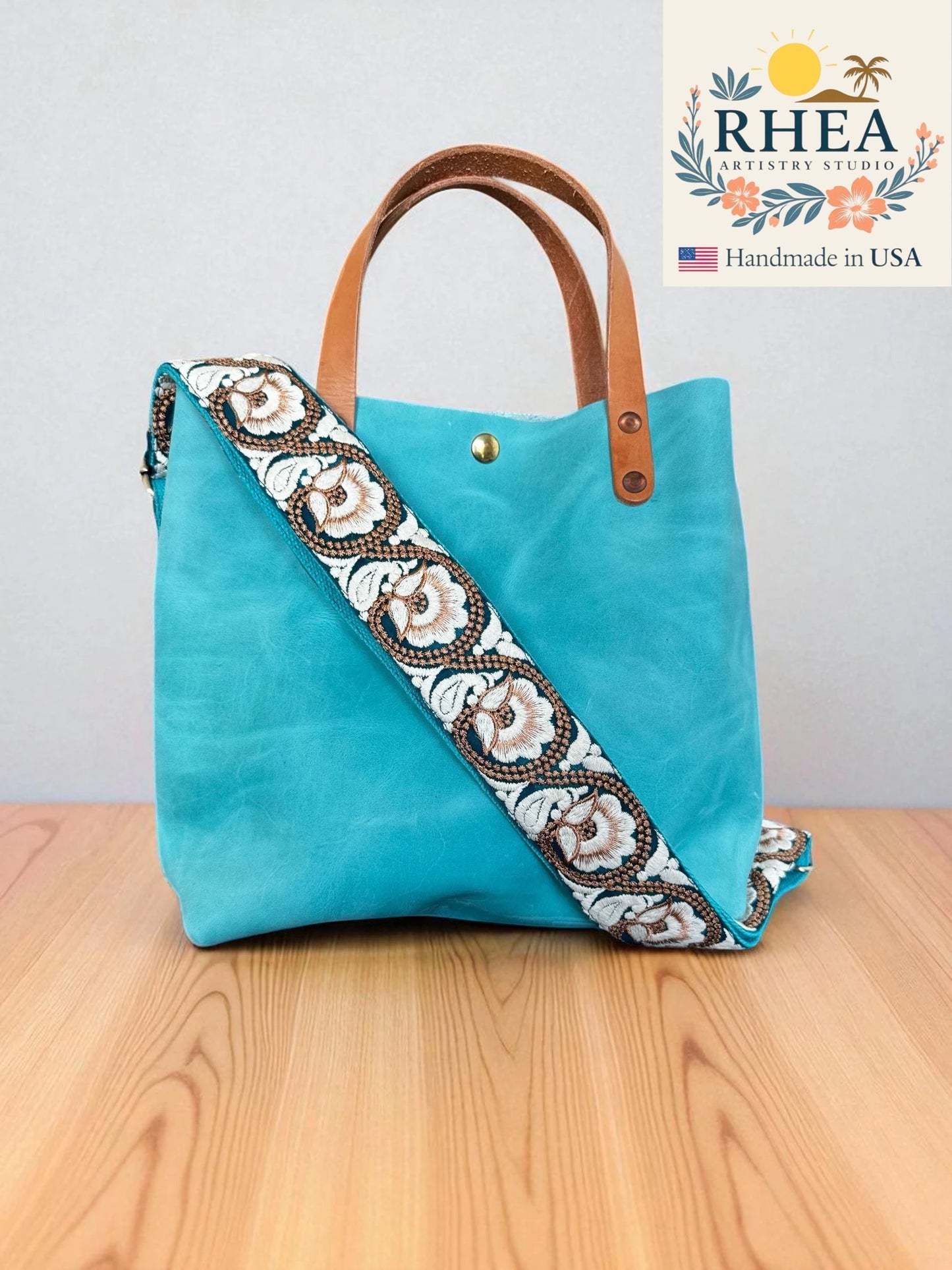 Turquoise handbag with decorative purse strap on a wooden surface, featuring the RHEA brand.