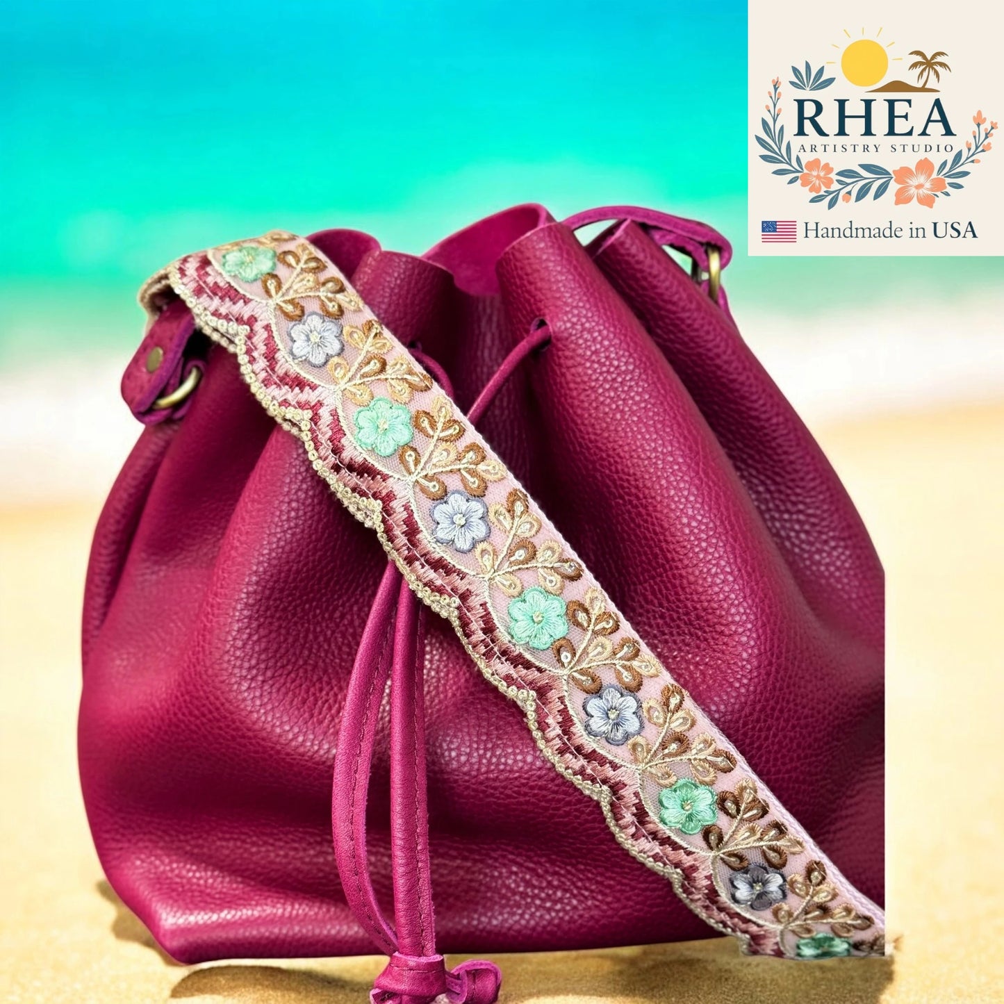 Pink leather drawstring bag with floral embroidery on a gradient background, featuring the RHEEA brand.