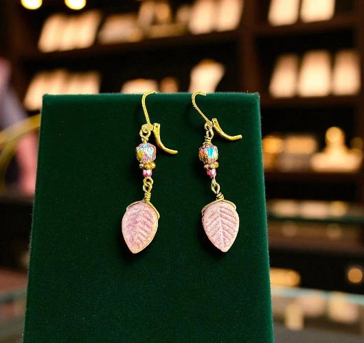 Pair of pink leaf-shaped earrings on a green stand with a blurred background