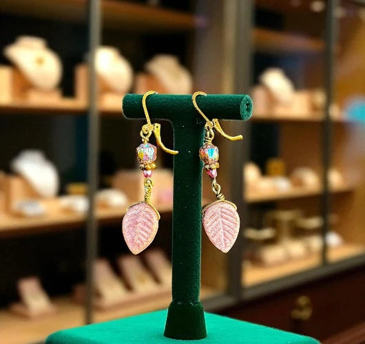 Pair of pink leaf-shaped earrings on a green stand with a blurred store background