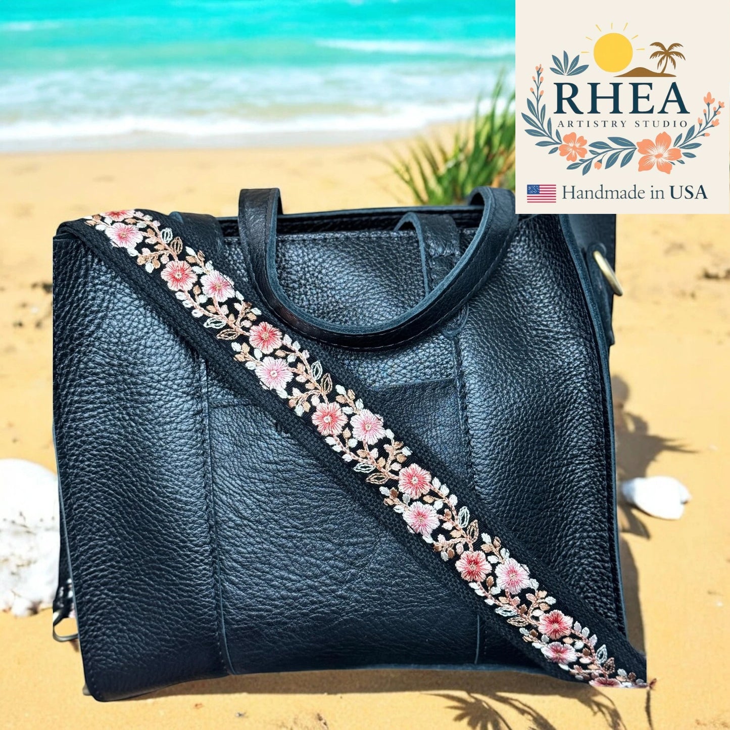 Black leather handbag with floral purse strap on a beach, featuring RHEA Artistry Studio logo.