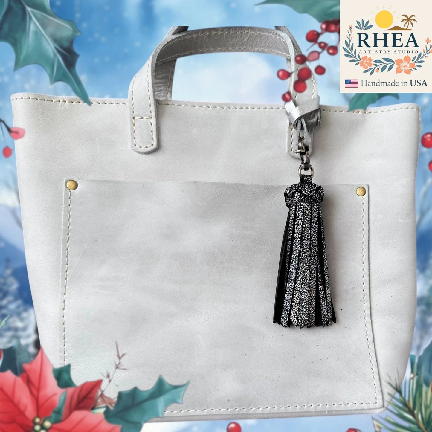 White handbag with a black tassel keychain on a decorative background with flowers and leaves.