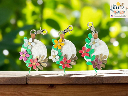 Three floral charms keychains on a wooden surface with a blurred green background
