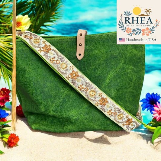 Green bag with floral purse strap on a beach background, featuring RHEA Artistry Studio logo.
