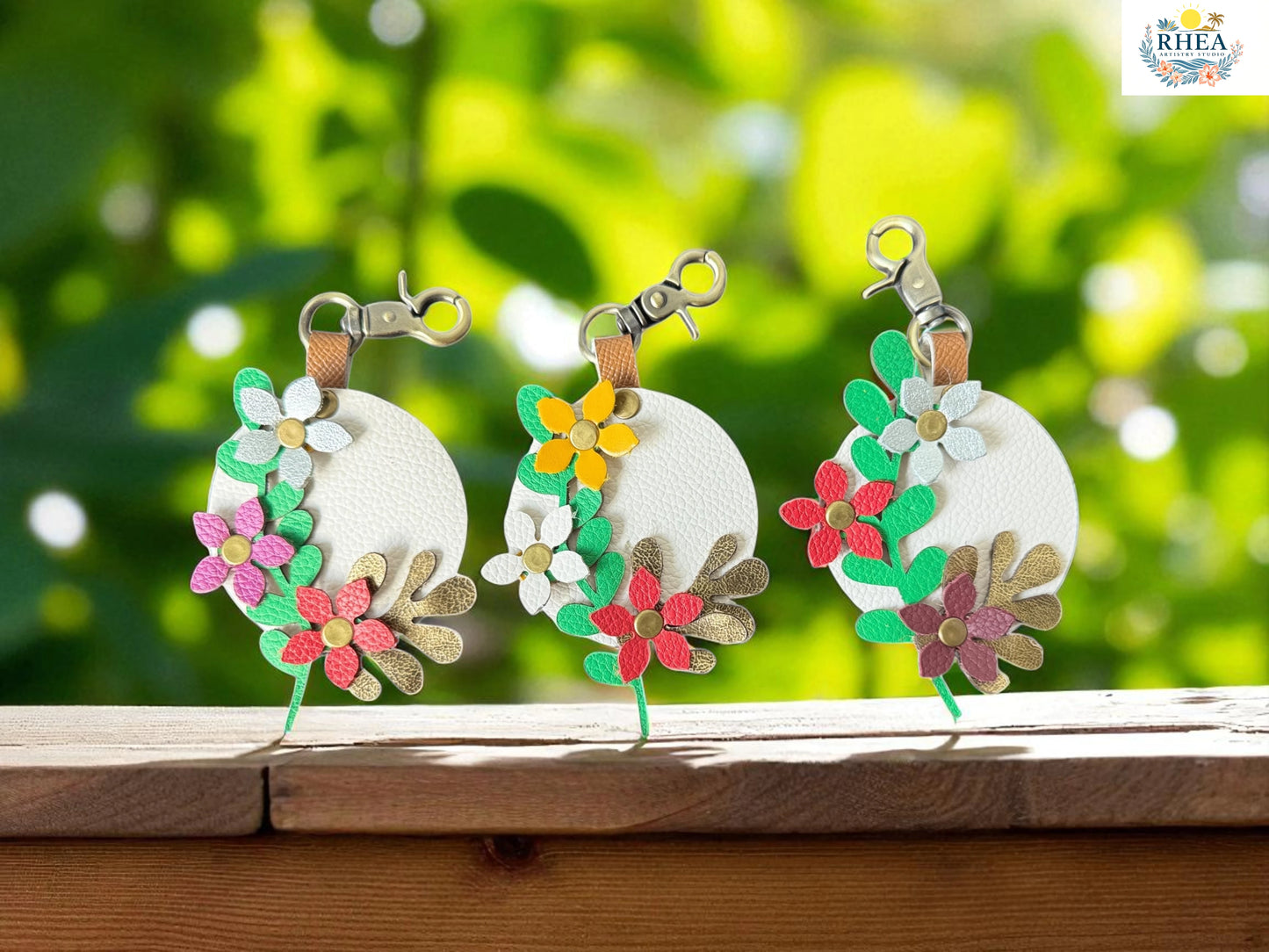 Three floral keychains on a wooden surface with a blurred green background