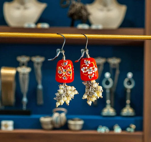 Red earrings with floral designs and pearl-like beads on a jewelry display.
