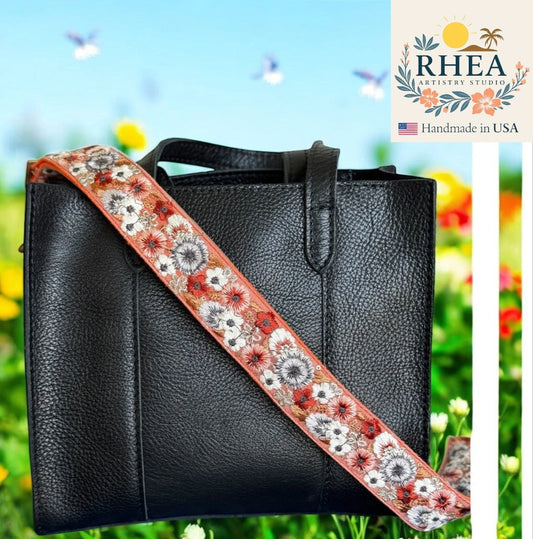 Black leather handbag with a floral purse
strap against a colorful outdoor background, featuring the RHEA Artistry Studio logo.