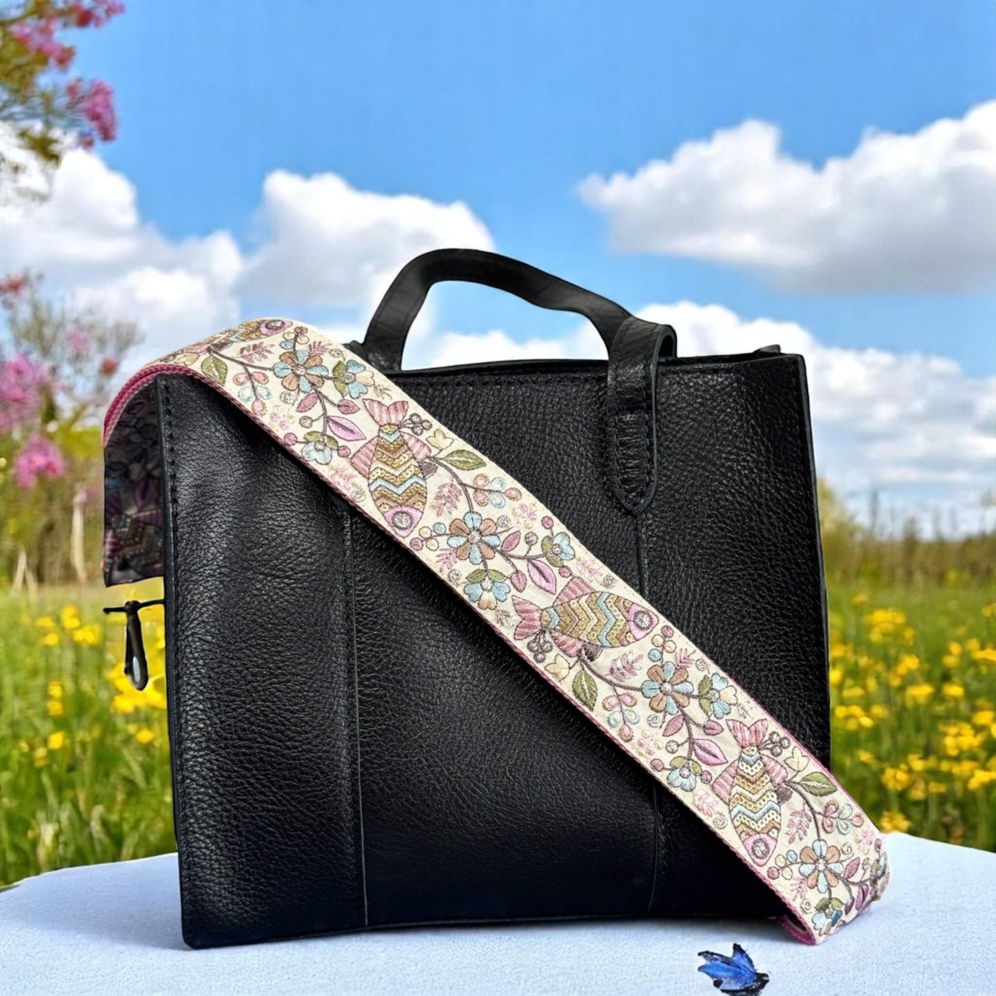 Adjustable embroidered purse strap with floral patterns and gold hardware, displayed on a gray background.