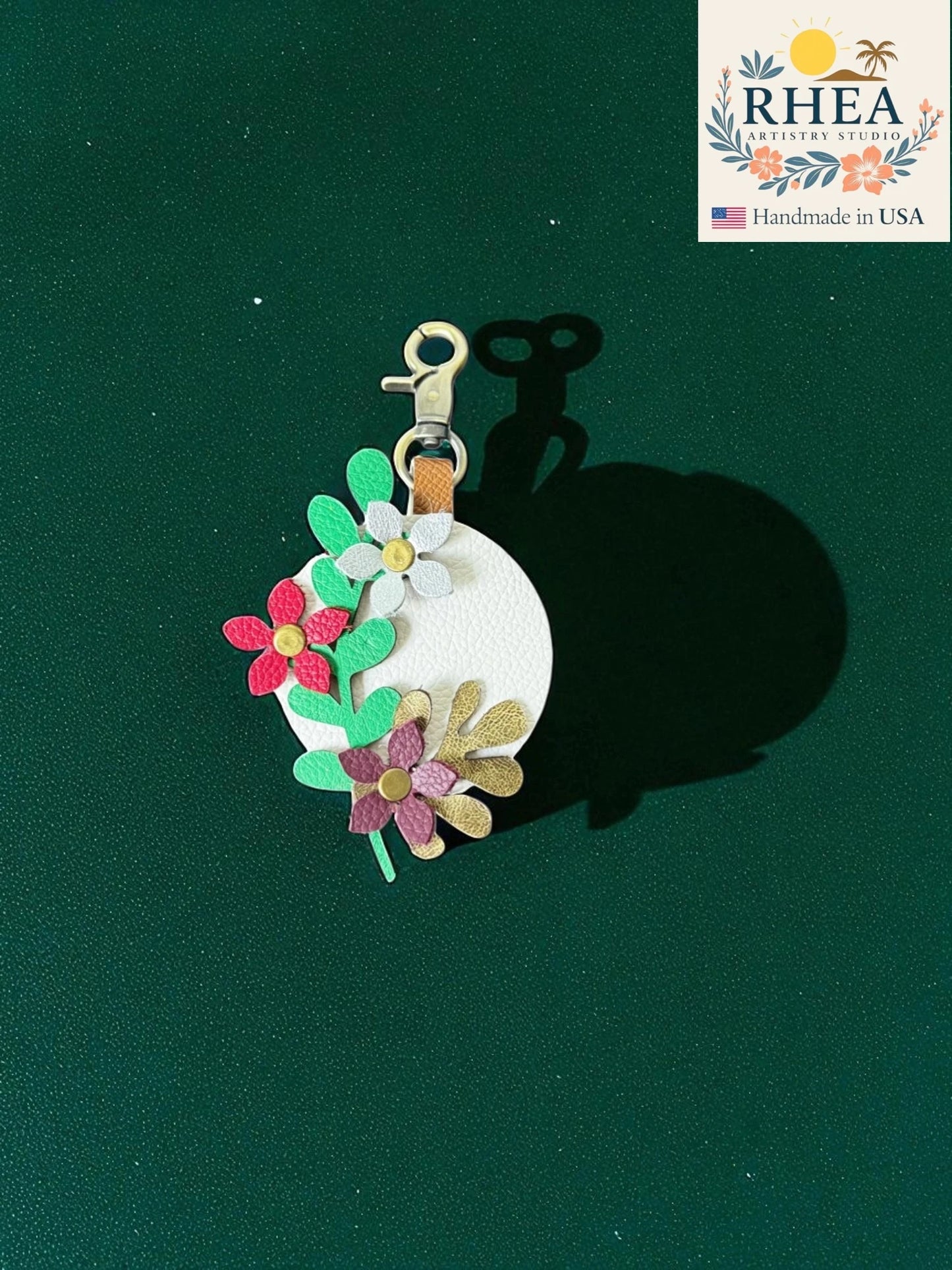 Floral leather bag charm on a green background with RHEA label.
