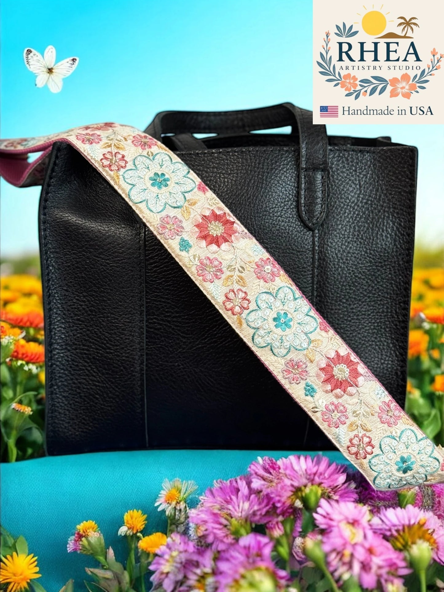 Black handbag with a floral purse strap against a colorful floral background, featuring the RHEA Artisan Studio logo.