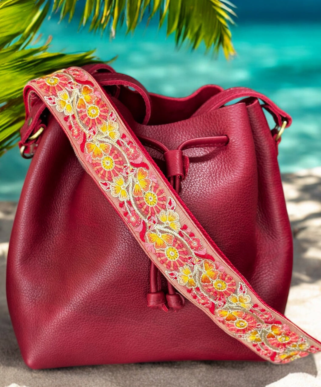 Red leather bag with a colorful floral strap on a beach