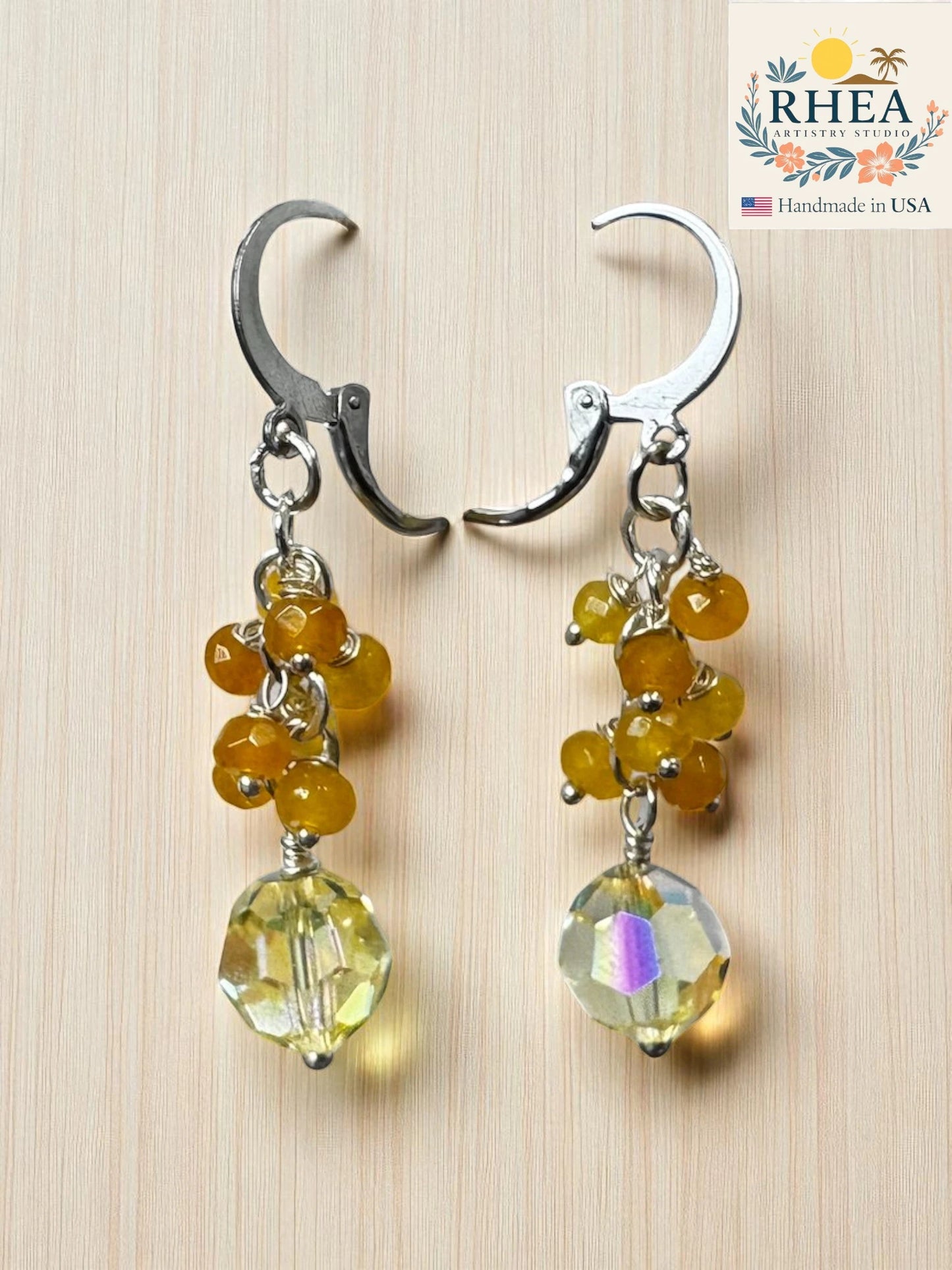 Pair of earrings for women with citrine beads and a large clear bead on a wooden surface, branded 'RHEA'.