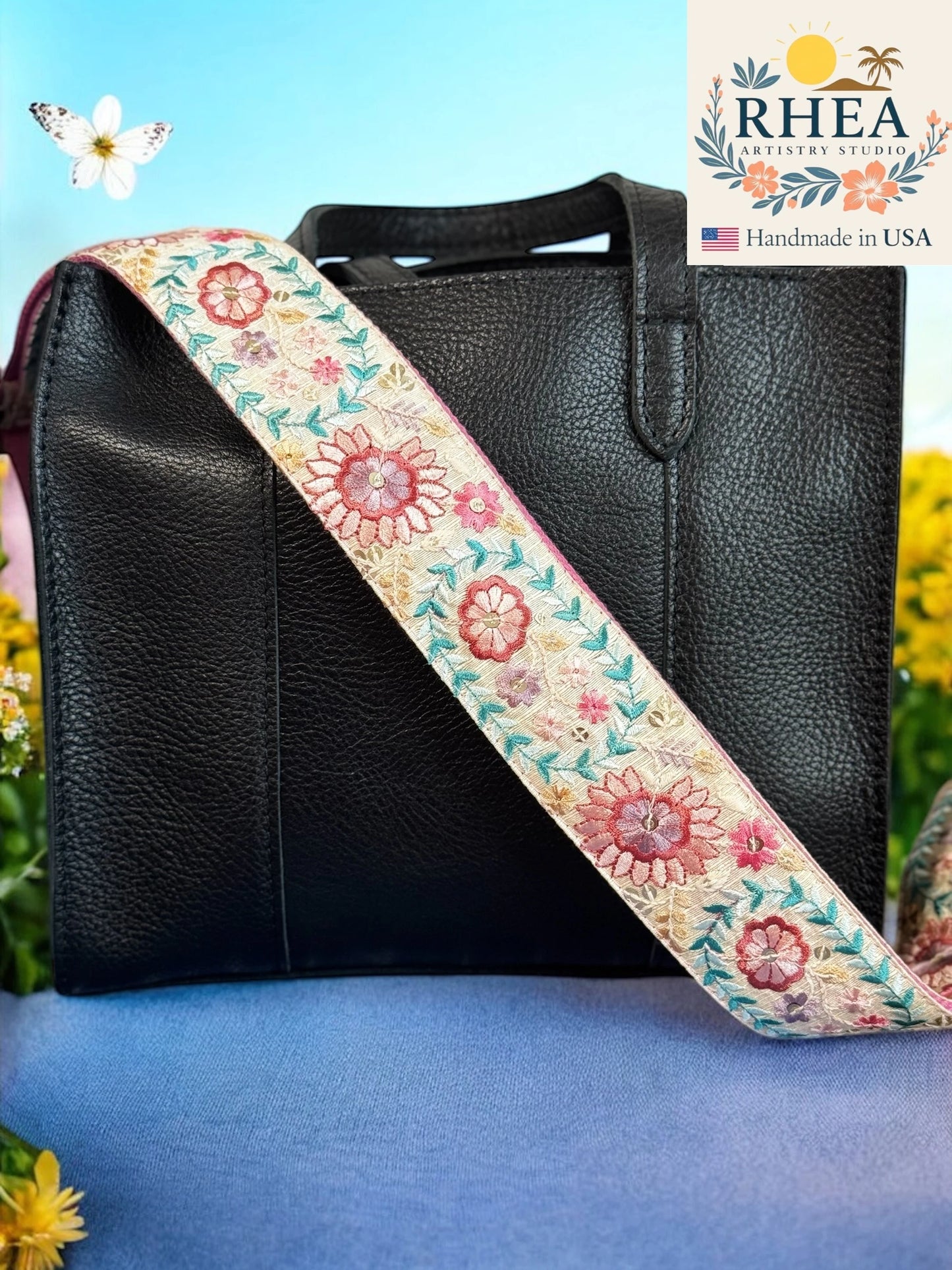 Black leather bag with a floral purse strap on a blue background, featuring the RHEA brand.