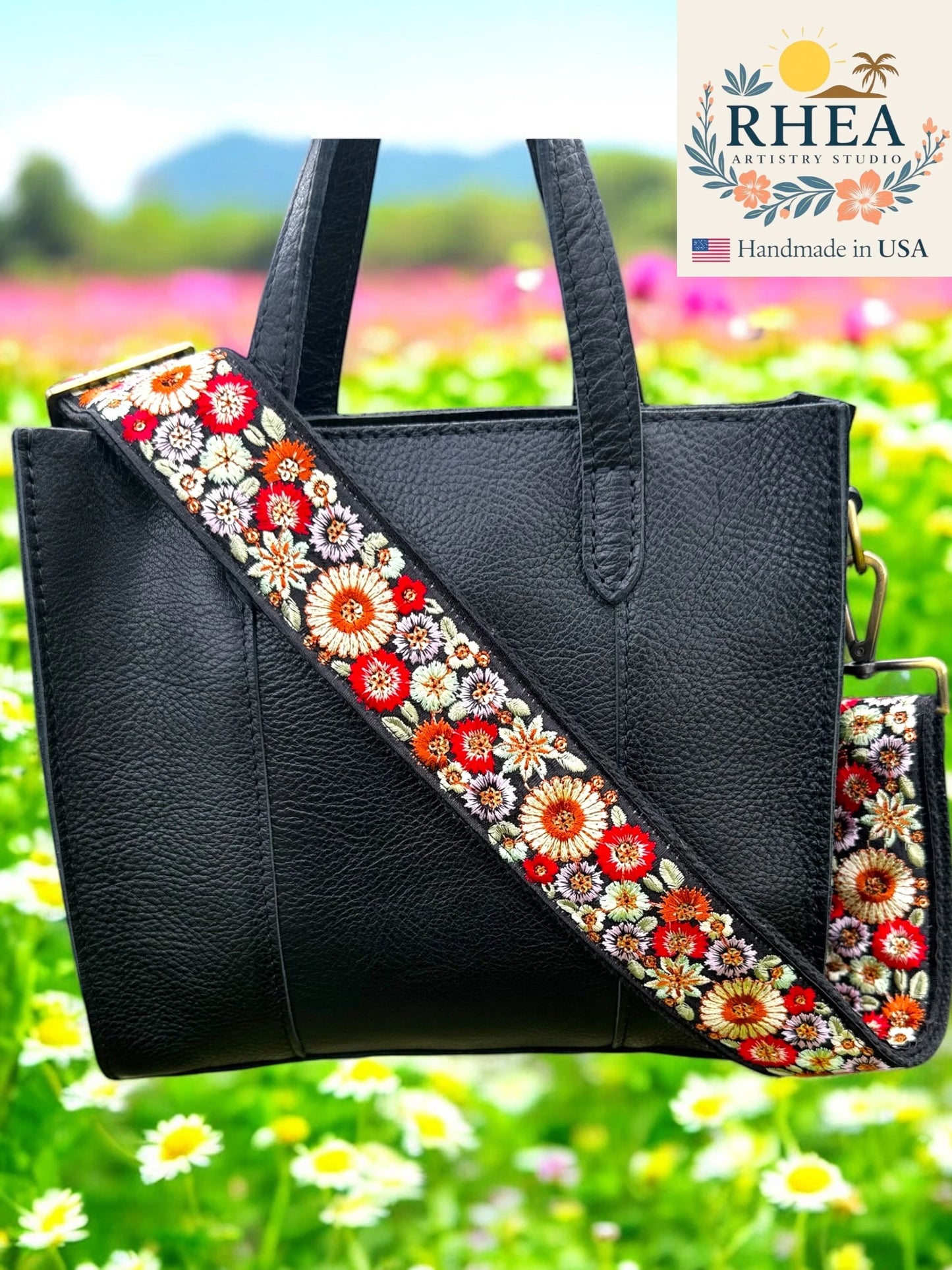 Black handbag with a floral purse strap against a colorful outdoor background, featuring the RHEA brand.