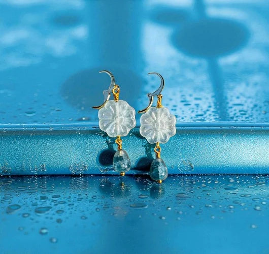 Floral earrings on a blue surface with water droplets