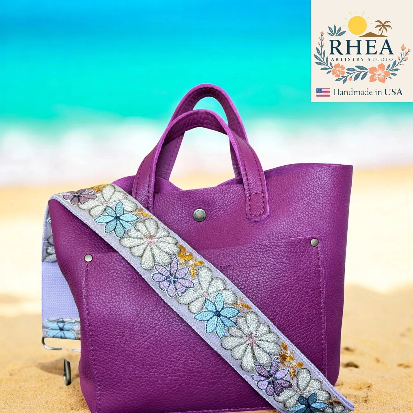 Purple handbag with a floral strap on a beach background, featuring the RHEA brand.