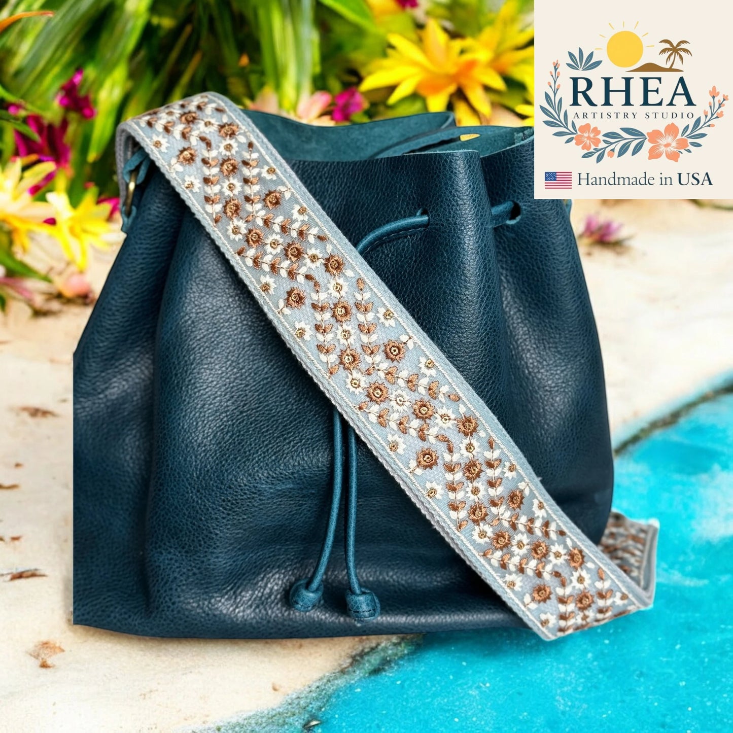 Blue leather bag with decorative purse strap against a natural background, featuring the Rhea Artistry Studio logo.