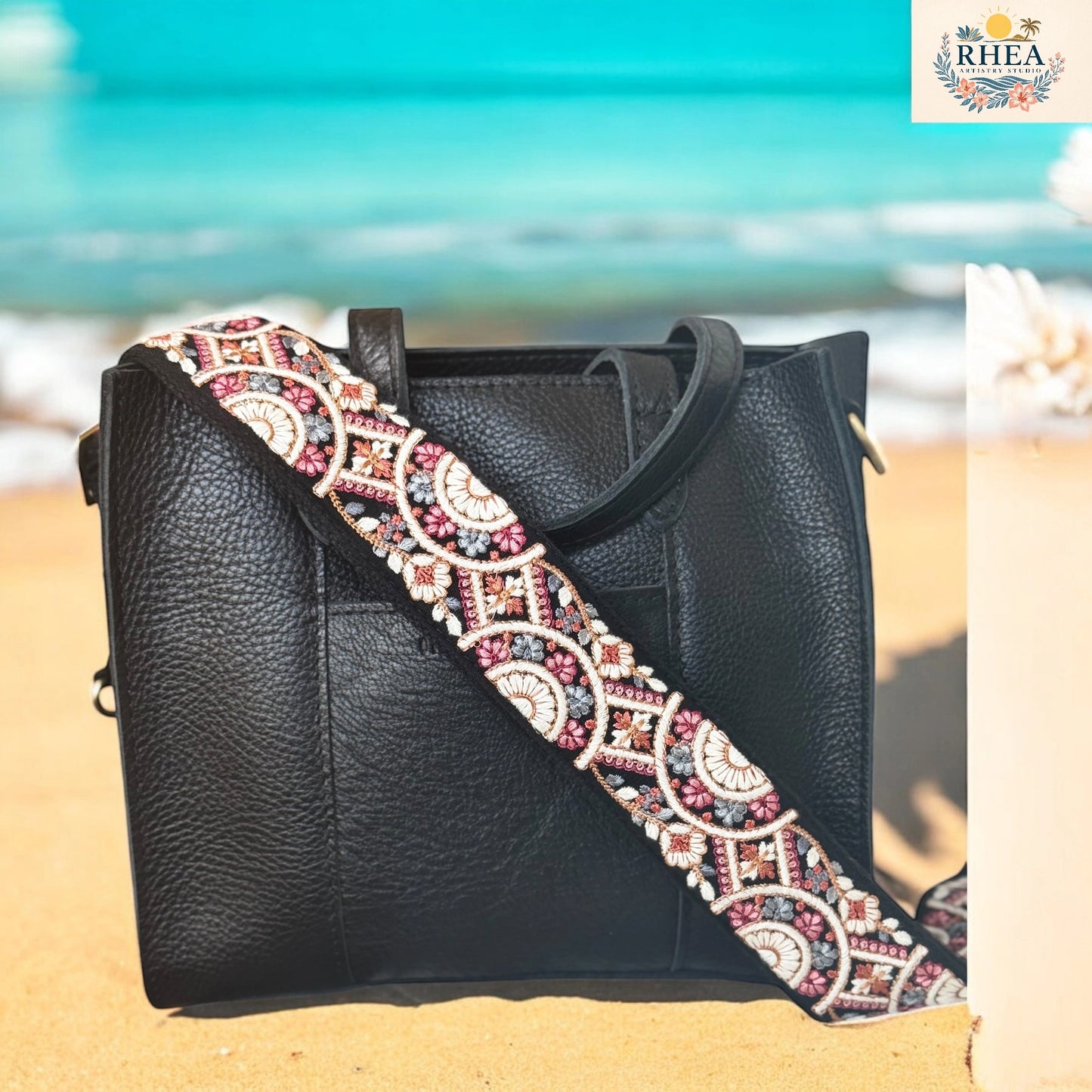 Black leather handbag with an embroidered strap on a beach