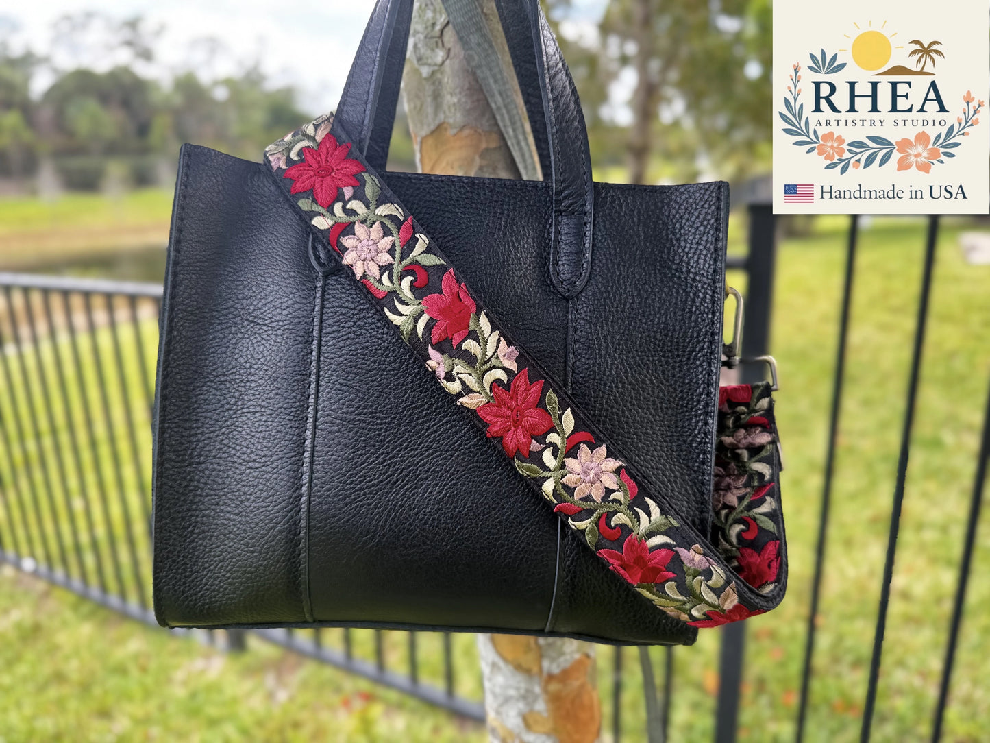 Black handbag with a floral purse strap in front of a blurred outdoor background