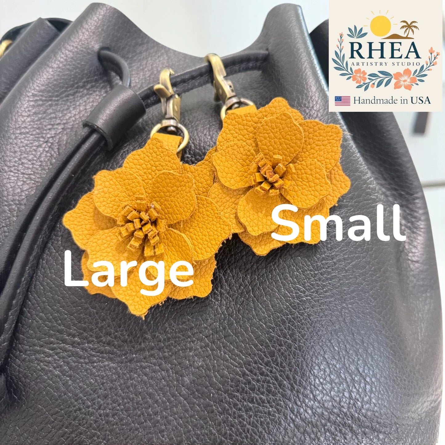 Yellow flower-shaped leather purse charms on a gray textured surface with 'RHEA' branding.