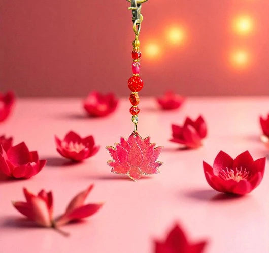 Pink lotus flower keychain with beads on a pink surface with red lotus flowers.