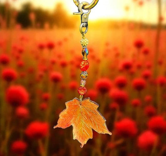 an orange maple leaf with a gold clasp on a natural maple leaf, with scarlet meadow in background