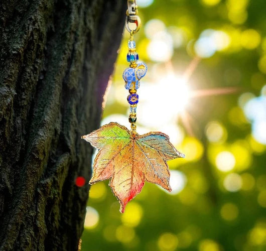 Decorative leaf charm with beads hanging against a blurred natural background