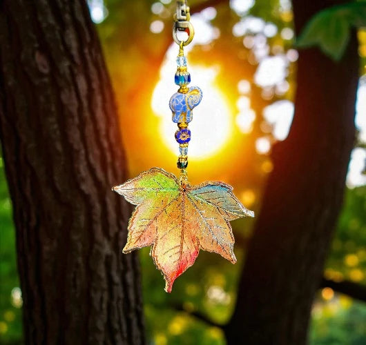 Colorful leaf-shaped keychain hanging from a tree with a blurred natural background
