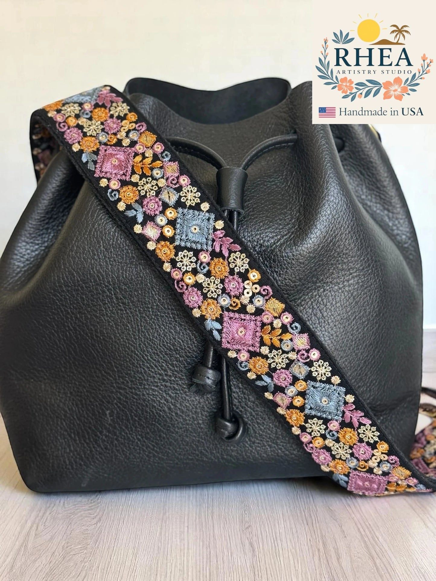 Black leather bag with a colorful beaded purse strap on a light wooden surface, RHEA brand visible.
