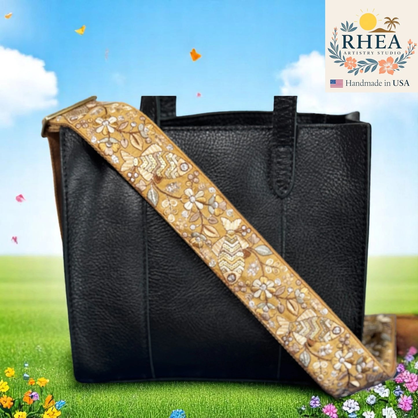 Black handbag with a decorative gold purse strap against a scenic background, featuring the RHEEA brand.