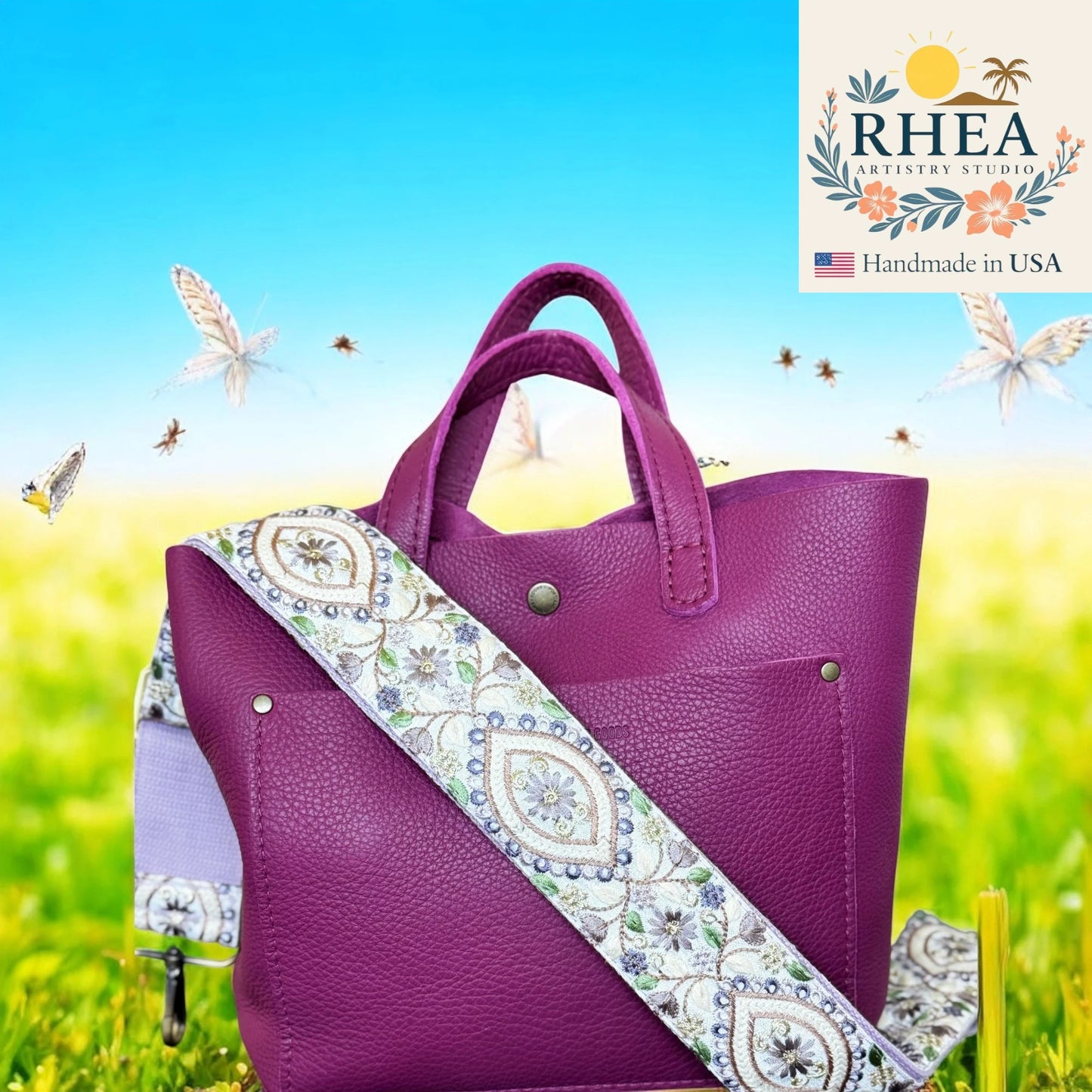 Purple handbag with a decorative strap on a grassy field background, featuring the RHEA Artistry Studio logo.