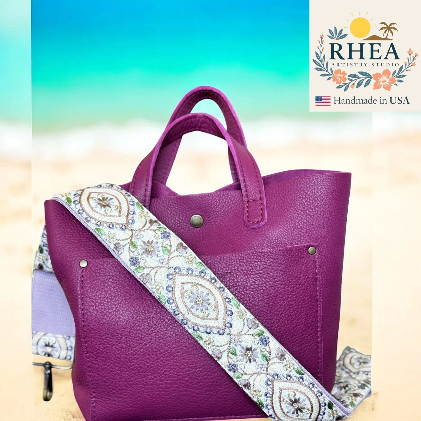 Purple handbag with a patterned strap on a beach background, featuring the Rhea Artistry Studio logo.