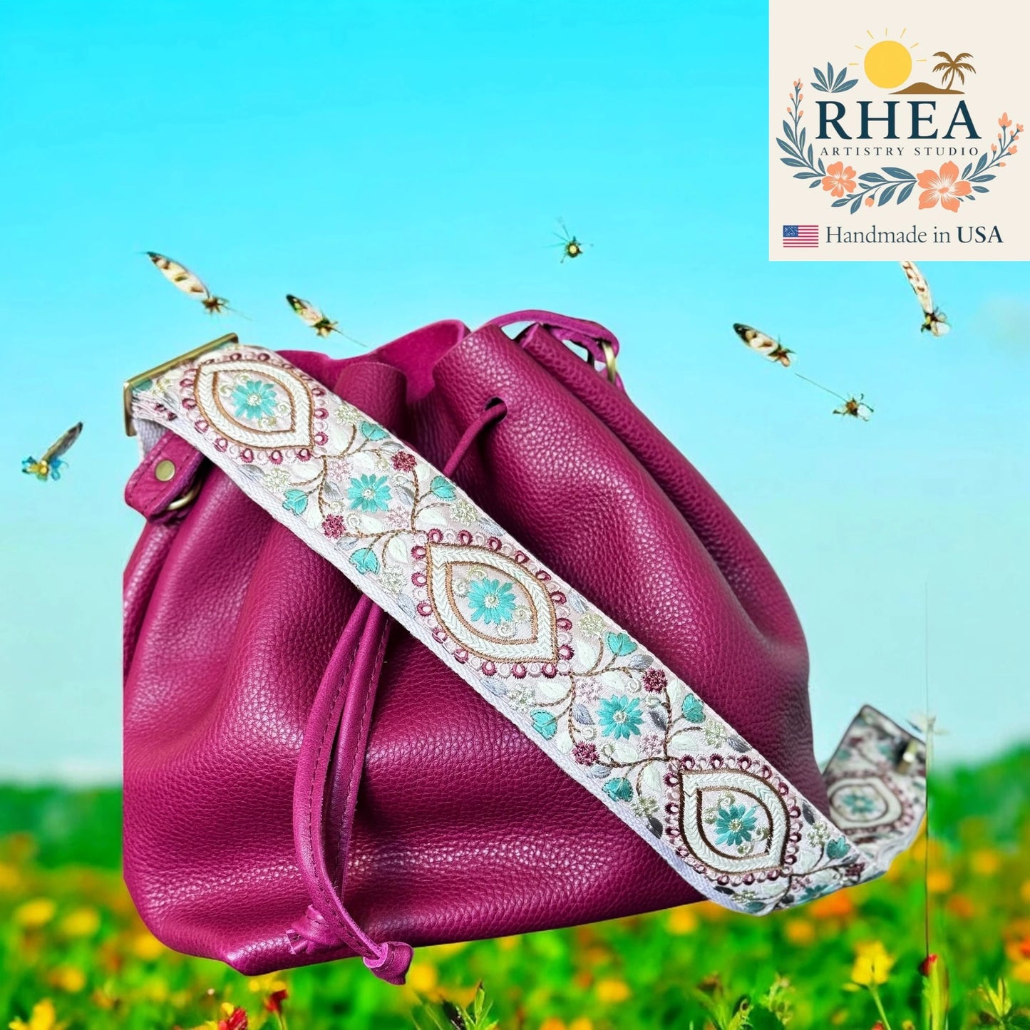 Pink leather bag with an embroidered strap on a scenic background, featuring the RHEA brand.