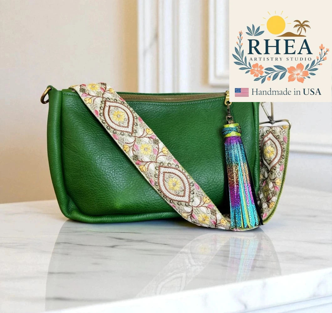 Green handbag with a colorful strap and tassel on a marble surface, featuring RHEA Artistry Studio logo.