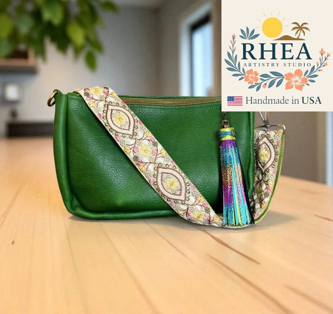 Green handbag with a patterned strap and tassel on a wooden surface, RHEA Artistry Studio logo visible.