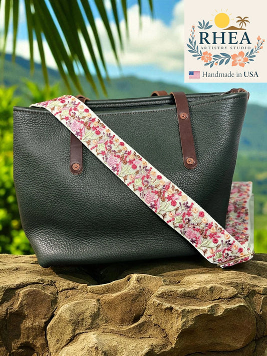 Black leather handbag with a floral purse strap on a rock, with RHEA branding above.