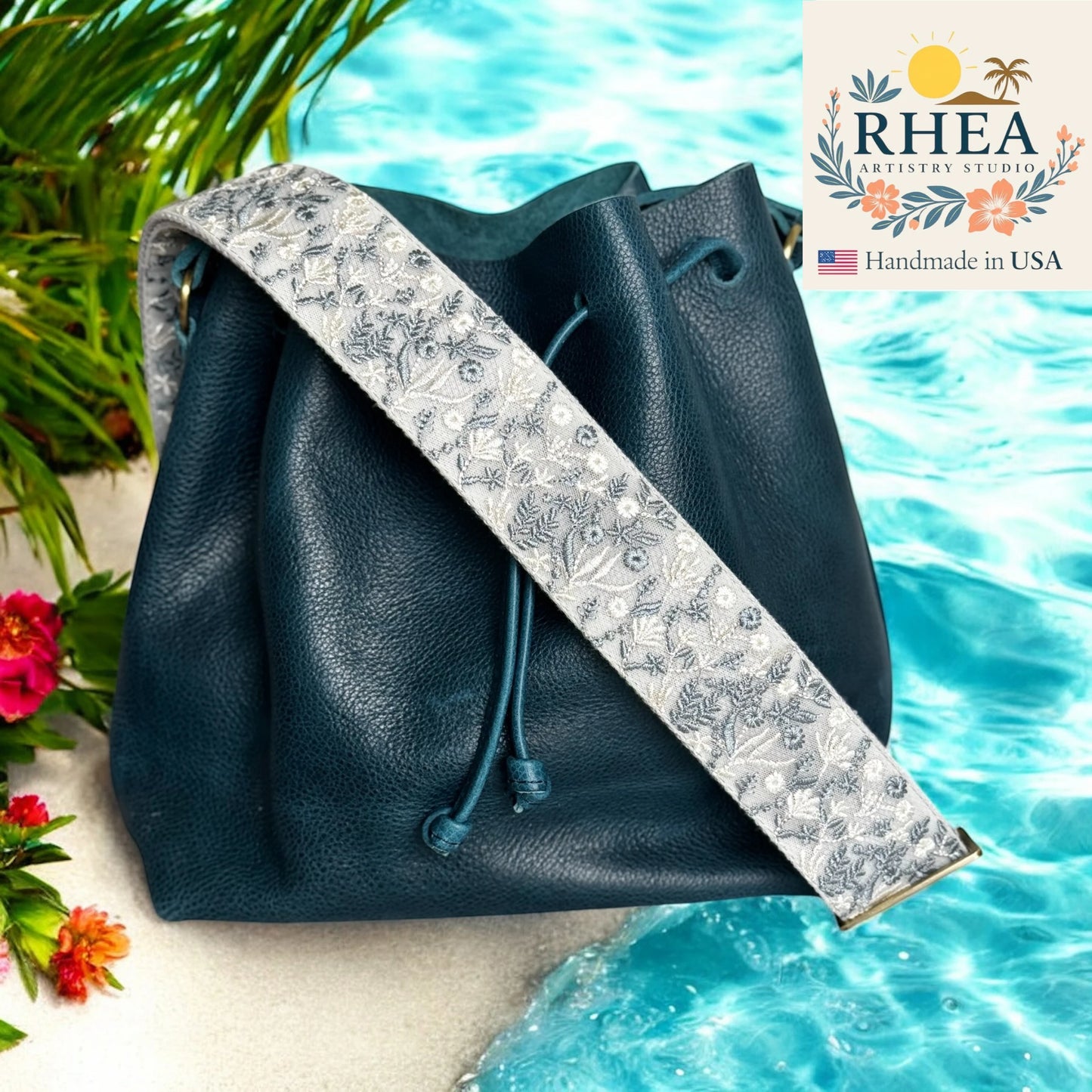 Blue leather bag with a floral purse strap by RHEA Artistry Studio against a poolside background.