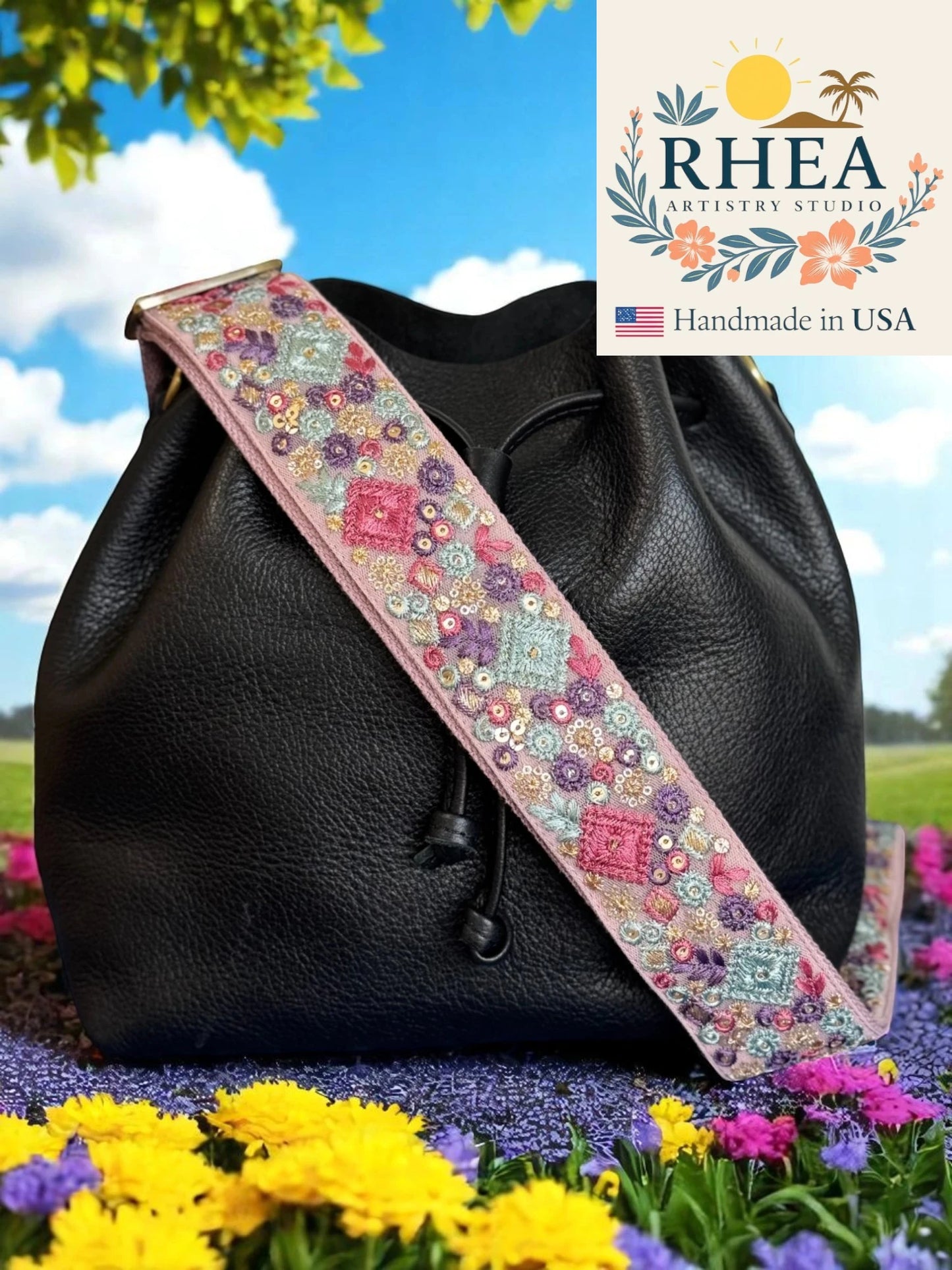 Black leather bag with a colorful floral purse strap in an outdoor setting, featuring the RHEA Artistry Studio logo.
