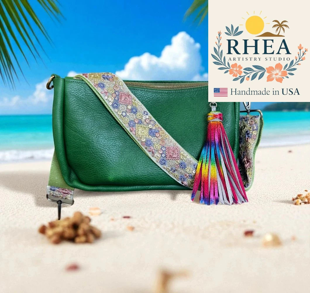 Green handbag with decorative purse strap and tassel on a beach, featuring RHEEA Artistry Studio logo.