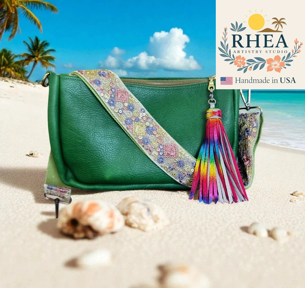 Green handbag with colorful tassel and purse strap on a beach, featuring RHEA Artistry Studio logo.
