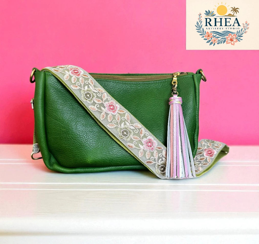 Green handbag with floral strap and tassel on a pink background, featuring the Rhea brand.