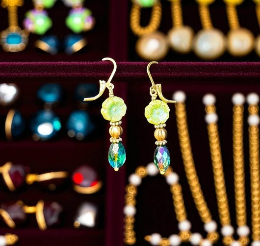 Pair of gold earrings with green and blue beads on a blurred jewelry display background.