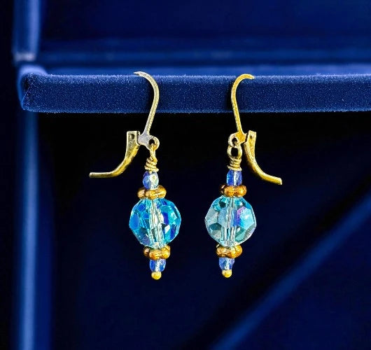 Gold and blue beaded earrings on a dark blue background