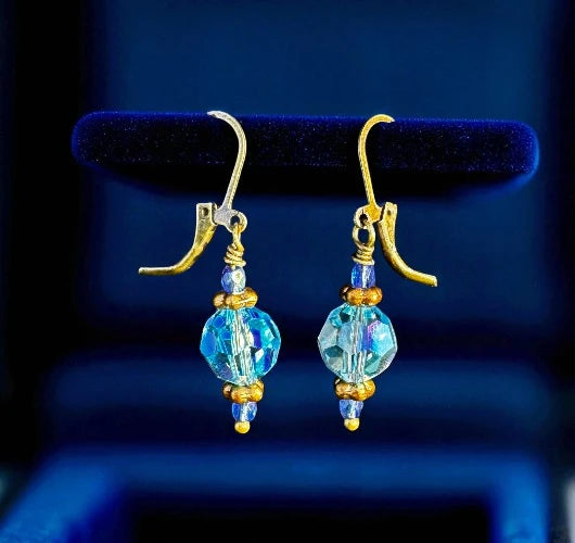 Gold and blue beaded earrings on a dark blue background