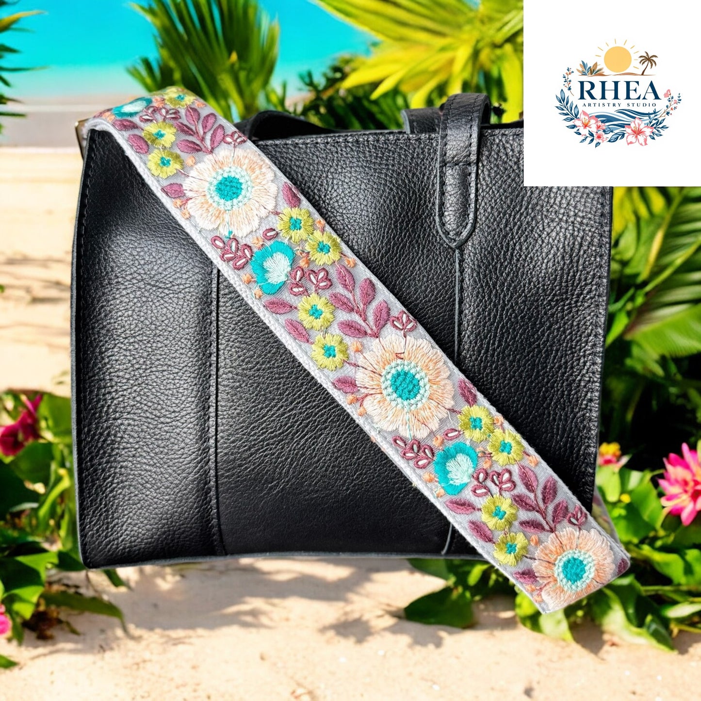 A black handbag with a floral strap featuring aqua, coral, and lavender embroidery. Set in a beach